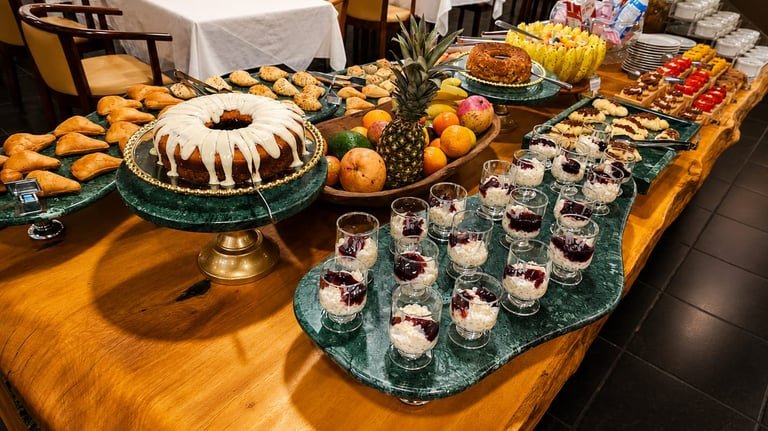 Outro ângulo do buffet com frutas inteiras, bolo e pequenas porções em taças